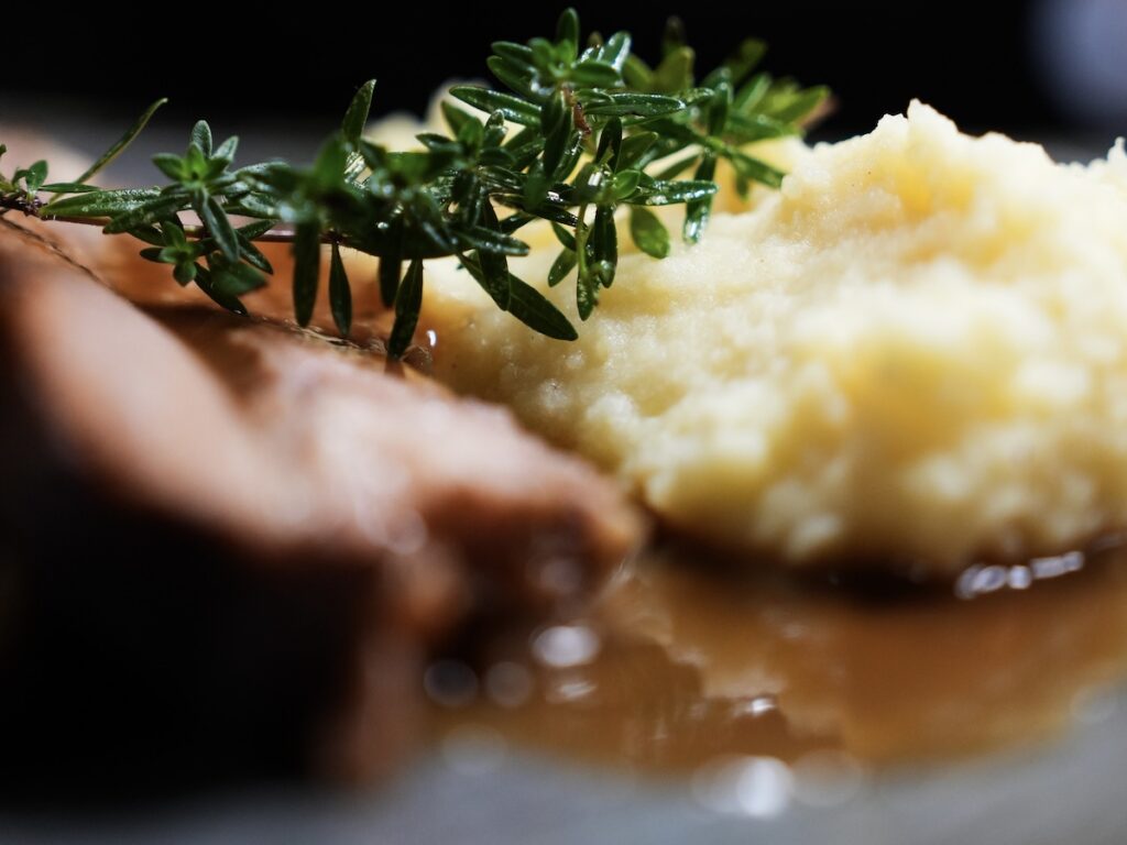 Fleischgericht mit Kartoffelpüree auf einem Teller mit frischen Kräutern